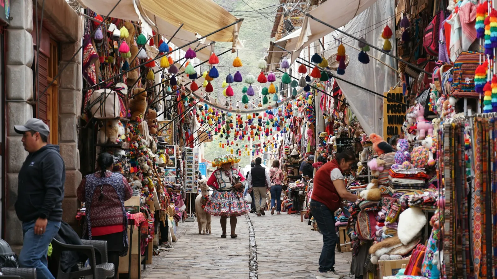 A street market in Pisac, Peru, with stalls of textiles, pompoms and alpaca soft toys along a cobblestone street