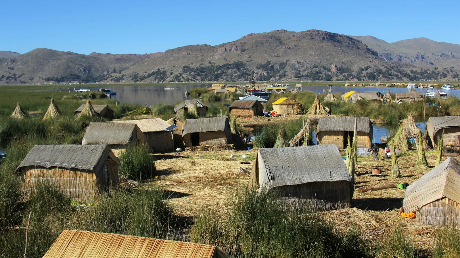 Reed houses on a floating island on Lake Titicaca, with water channels and dry hills behind
